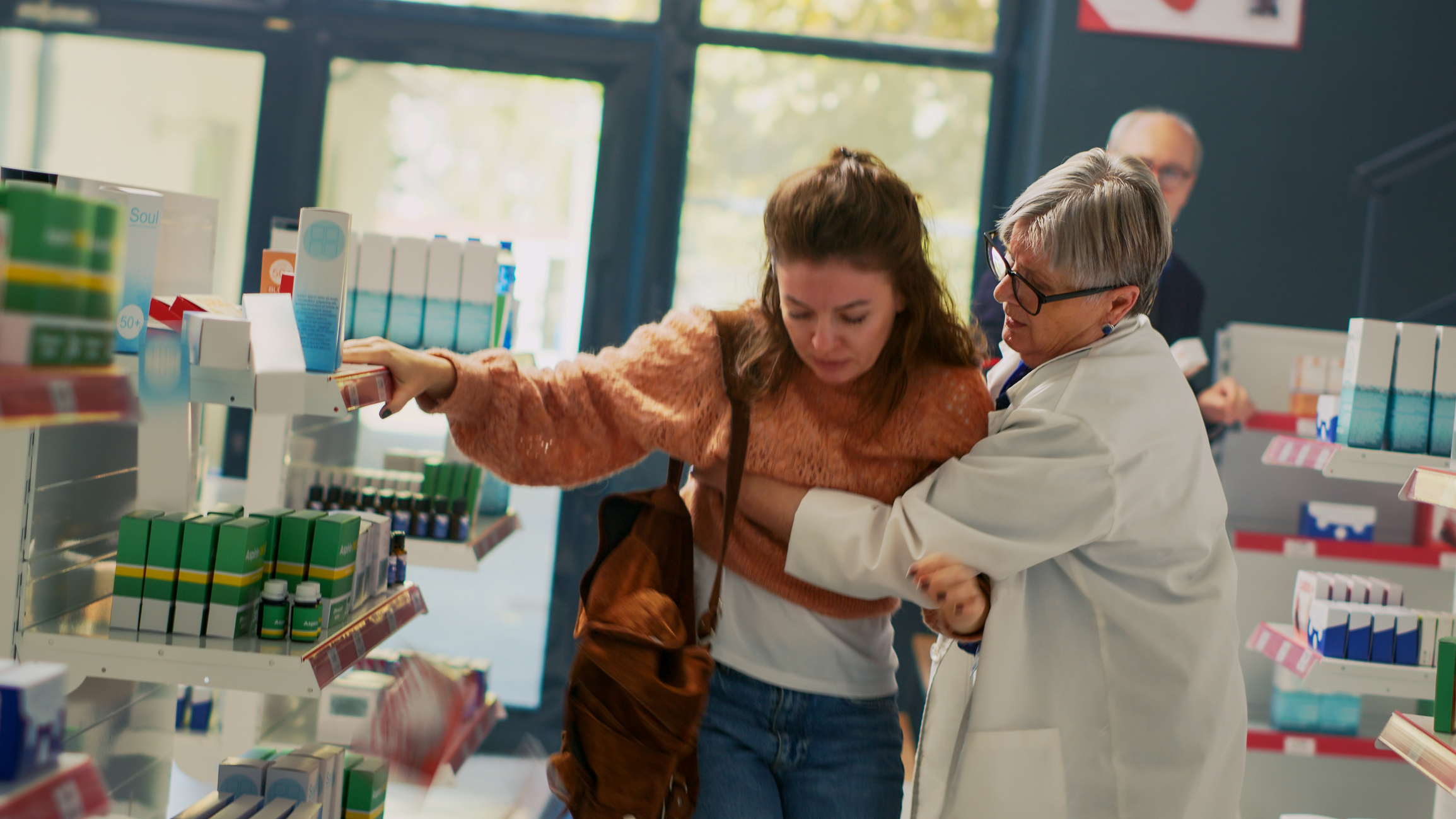 A concerned female pharmacist with short white hair recognizes early stroke symptoms when she holds a young white woman in an orange sweater to keep her from falling