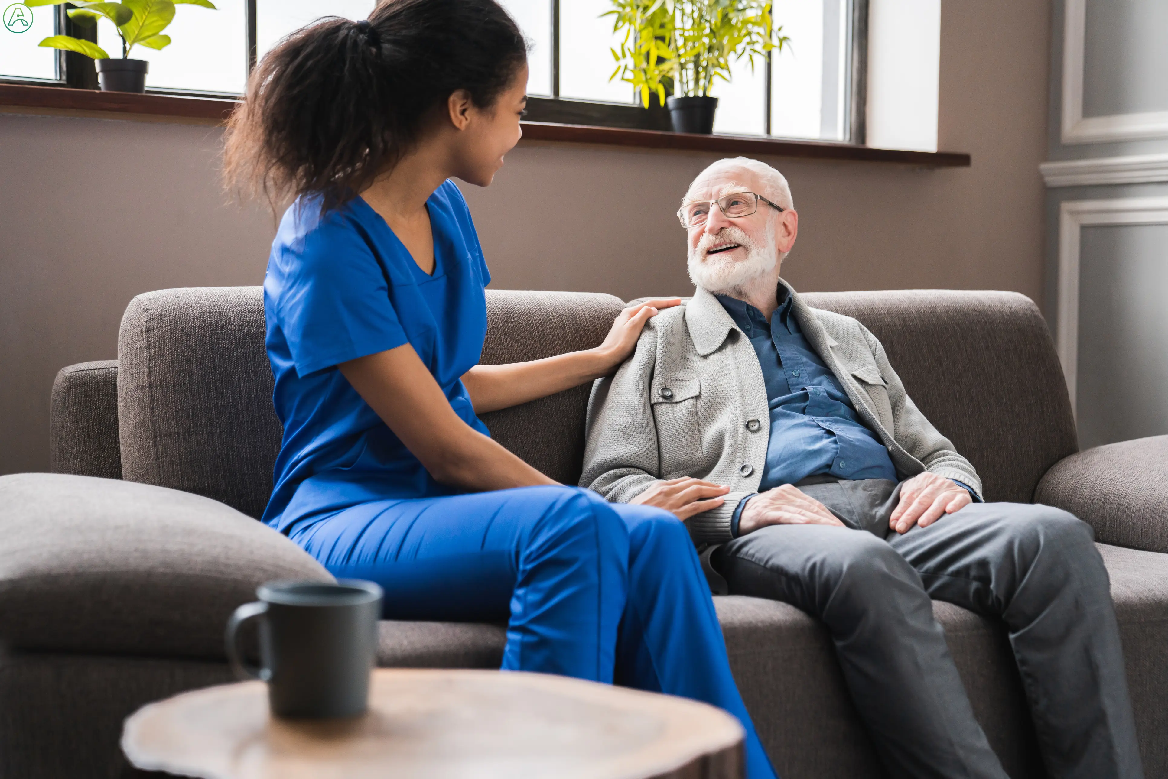 Young Black nurse assists a senior white man who sits and looks up at her.