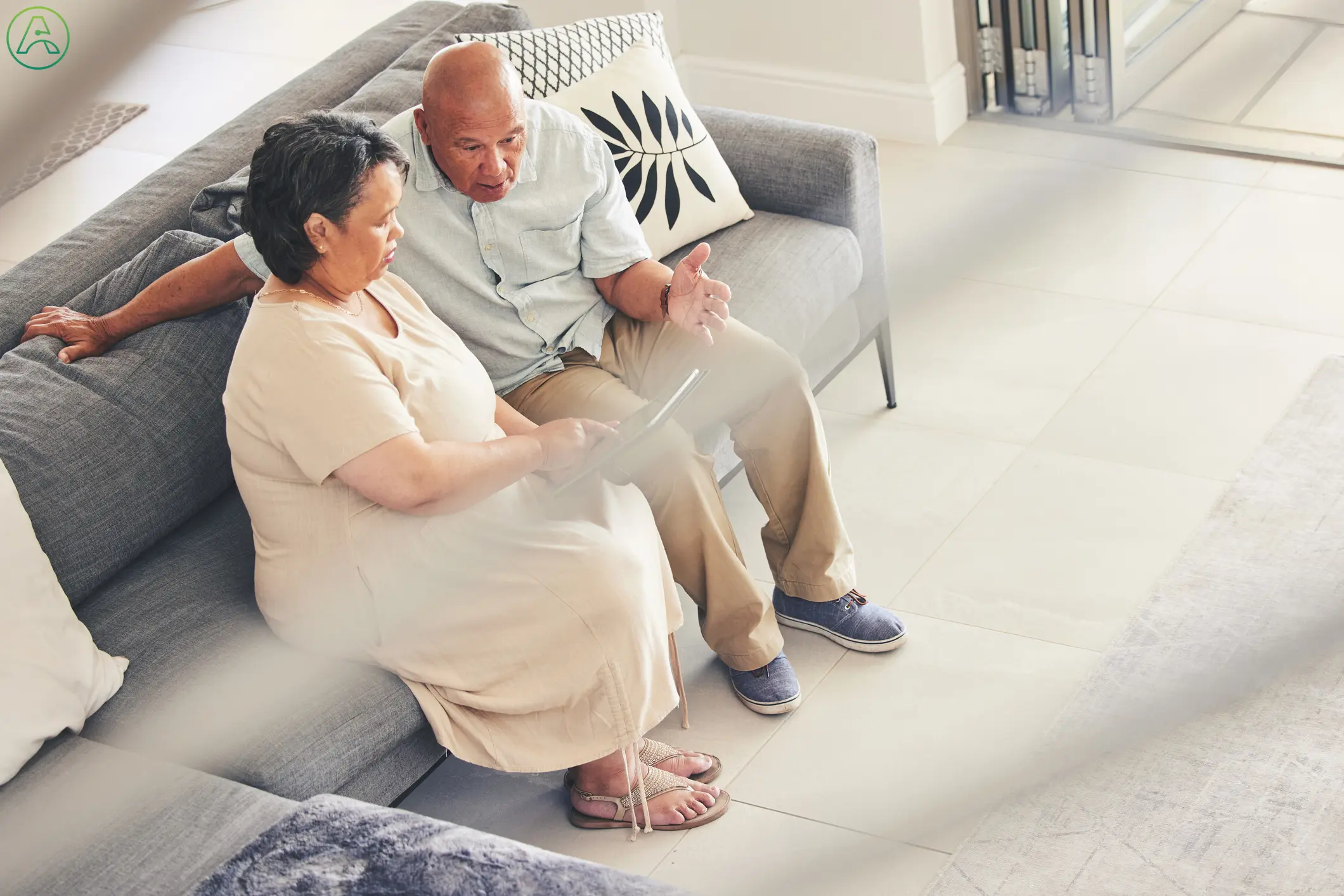 A middle aged man and woman sit on a couch at home, frustrated by a tablet with confusing accessibility settings.