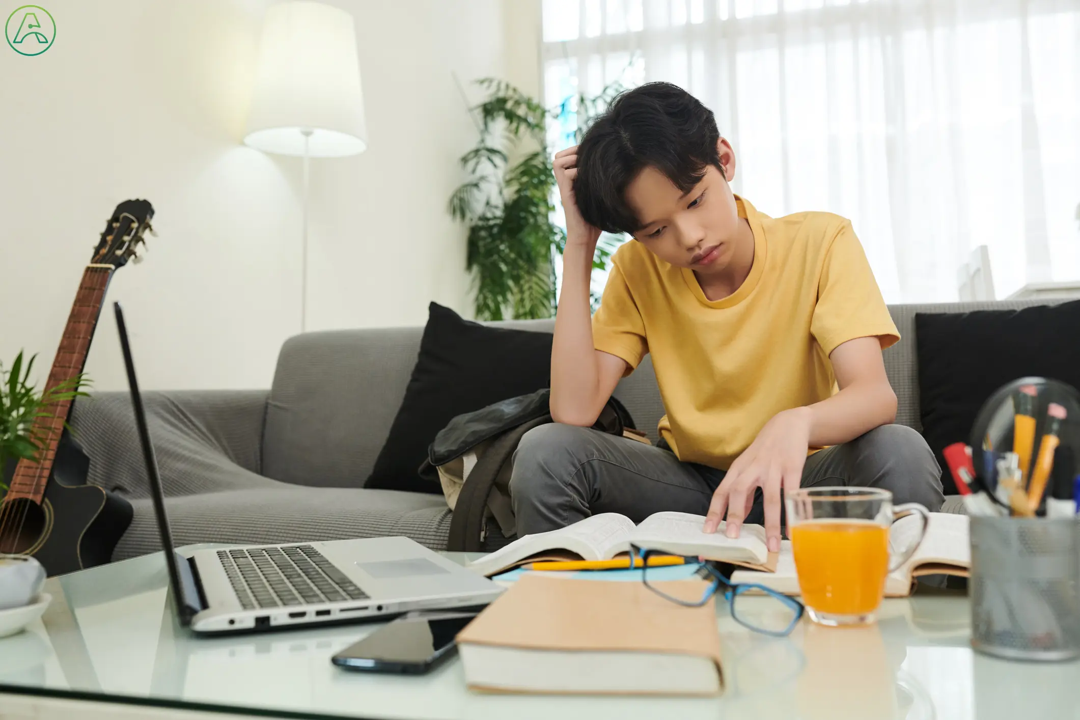 A teenage boy in a yellow shirt and gray pants scratches his head, frustrated with his homework.