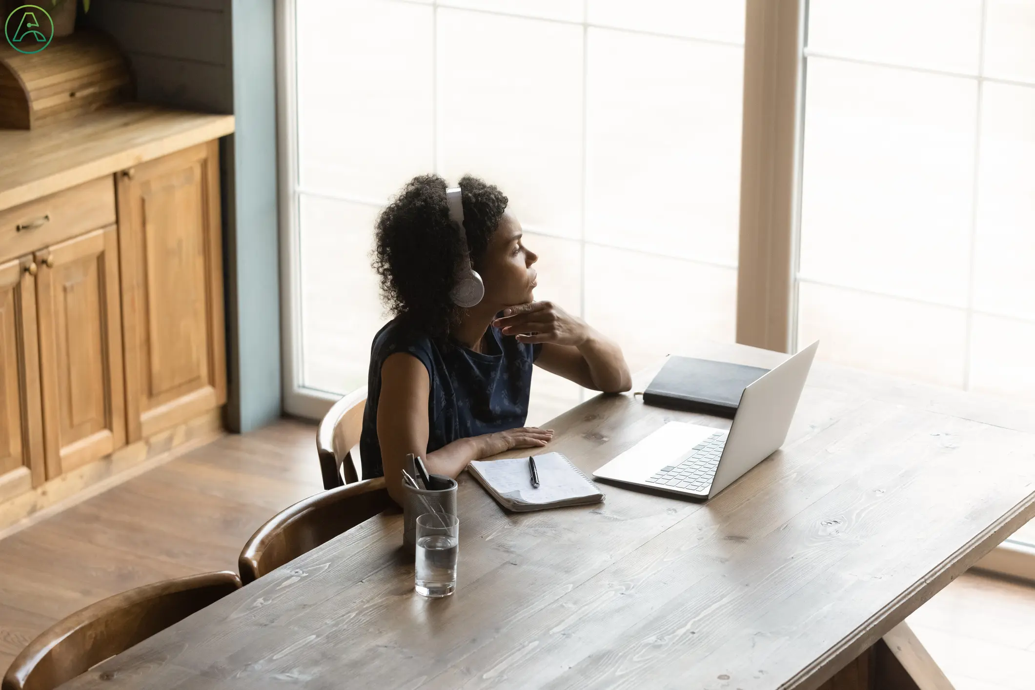 A Black woman works from home at her clean dining room table, wearing headphones to cancel out the distracting sounds of tinnitus.