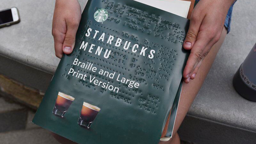 Hands holding the new Starbucks menu in braille