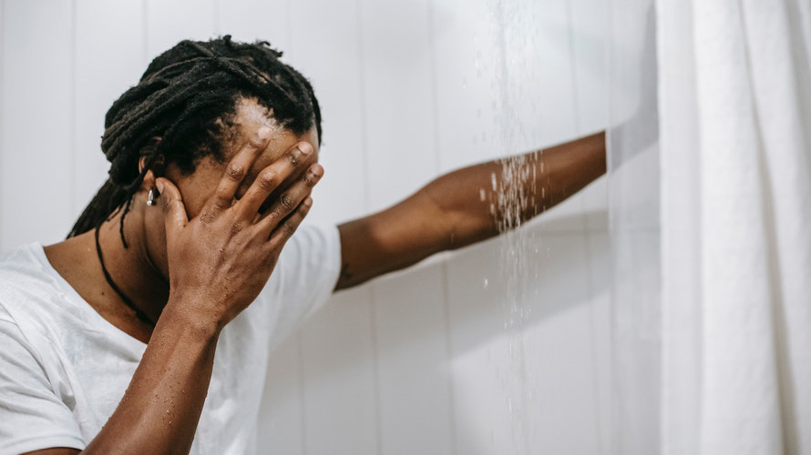 Person standing with arm propping them up in a shower holding their face in pain