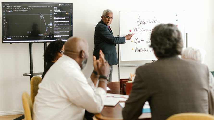 Older man pointing to a whiteboard leading a meeting or training
