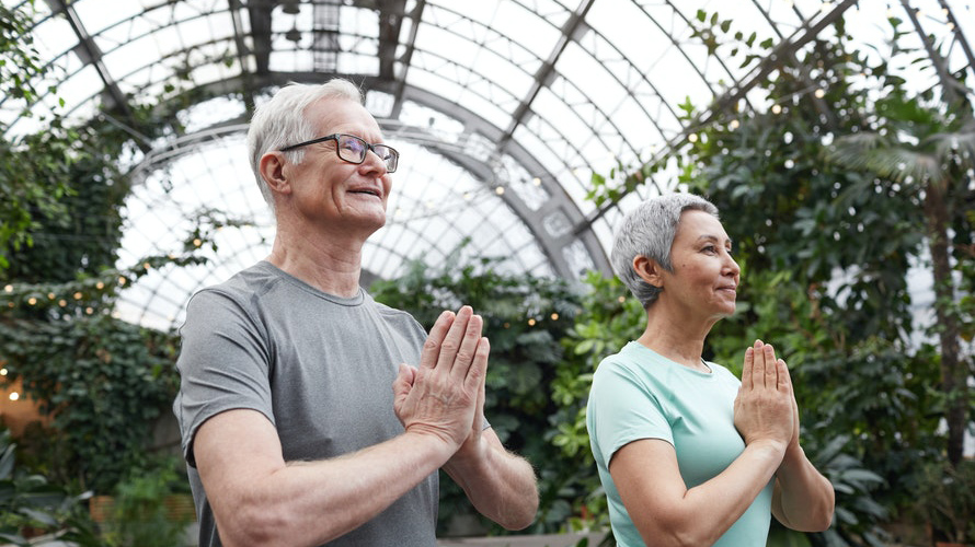 Older woman and man doing yoga in a conservatory