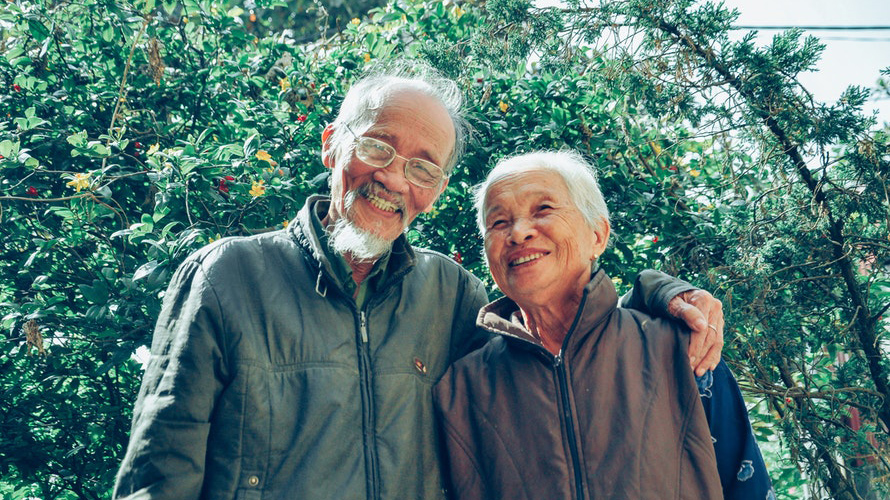 Happy older couple standing in front of a bush