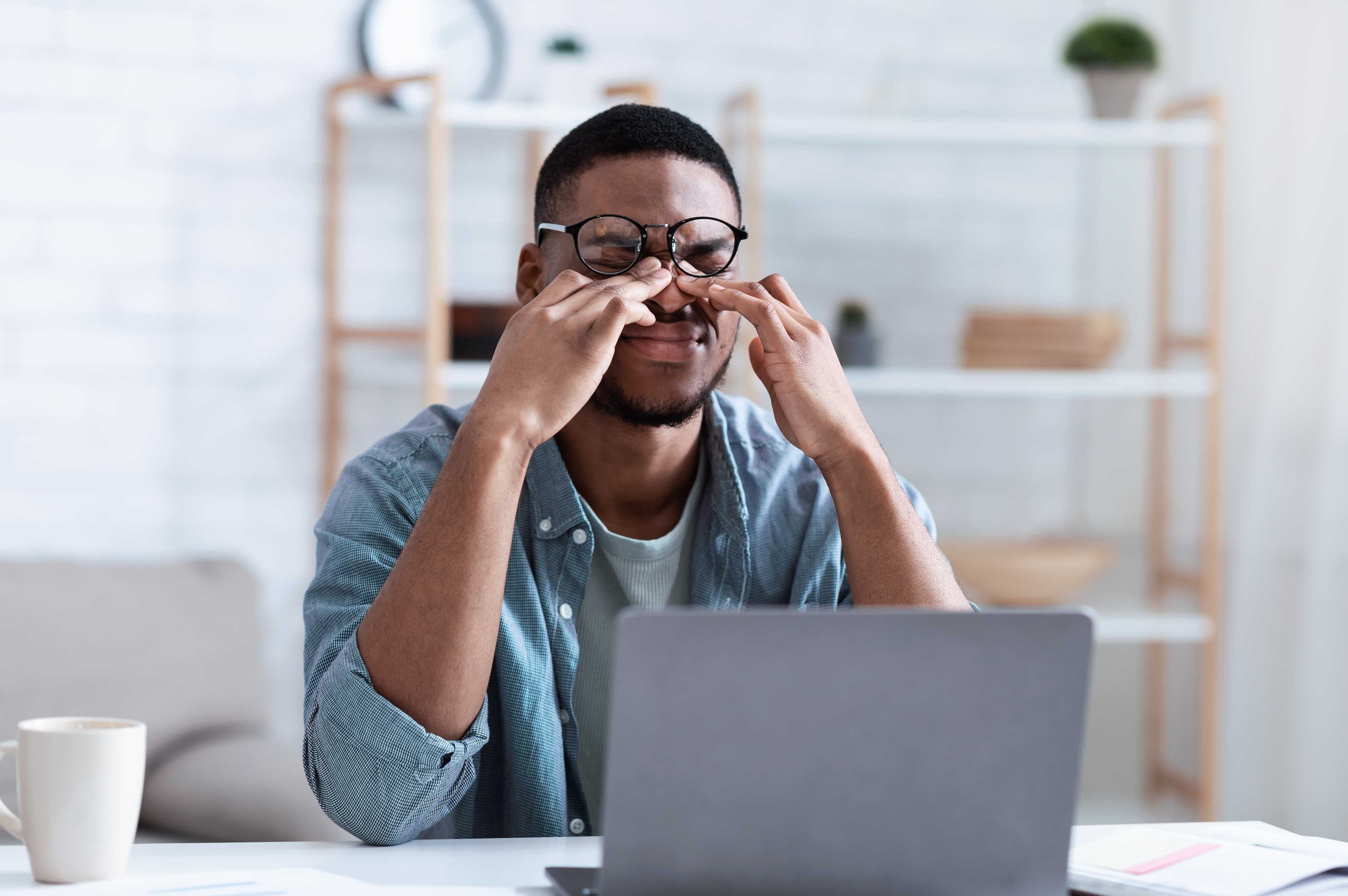 Black man sits at a laptop computer and rubs his eyes