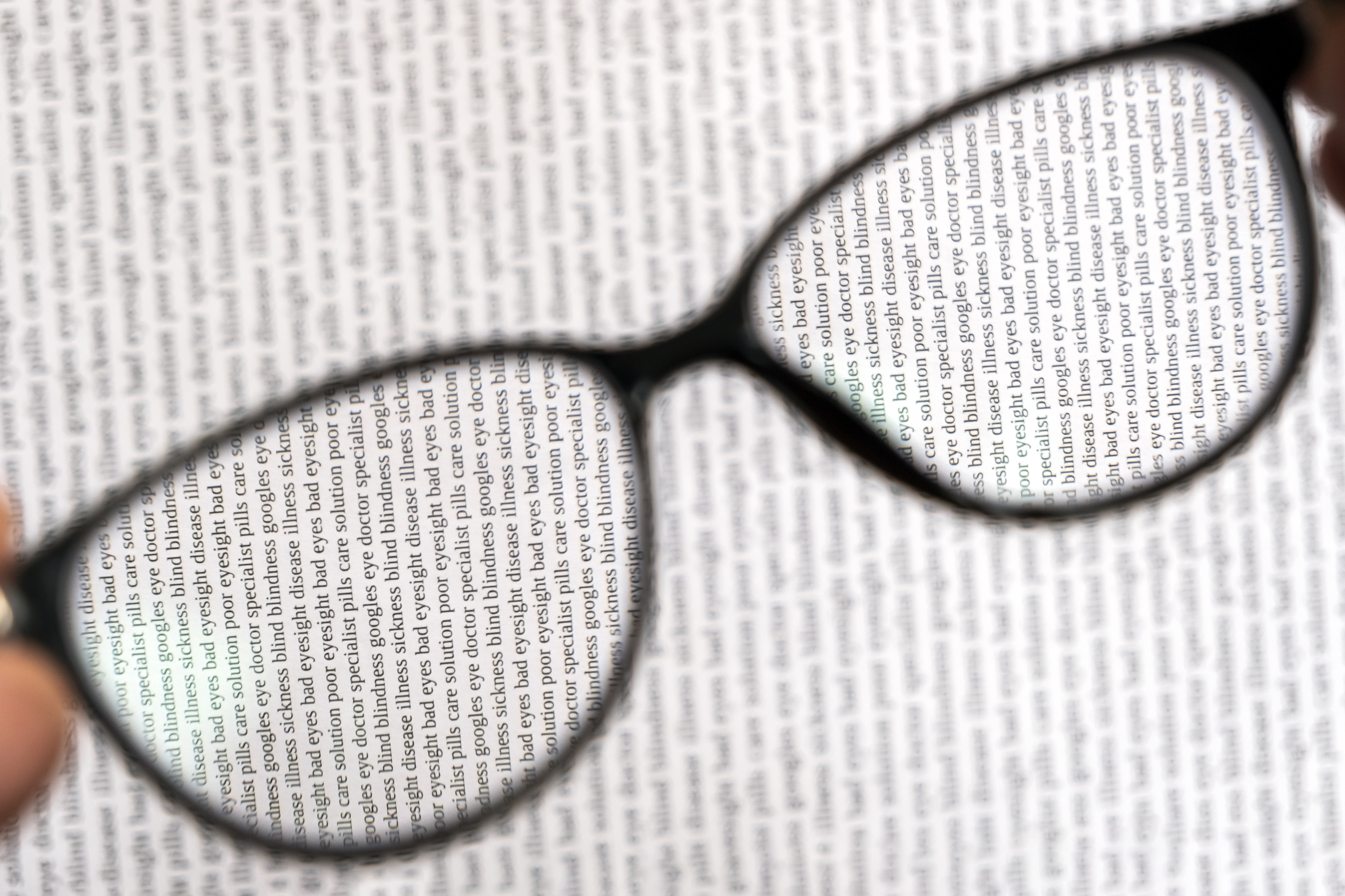 glasses are held above small print letters in a book, sharpening up the blurry text