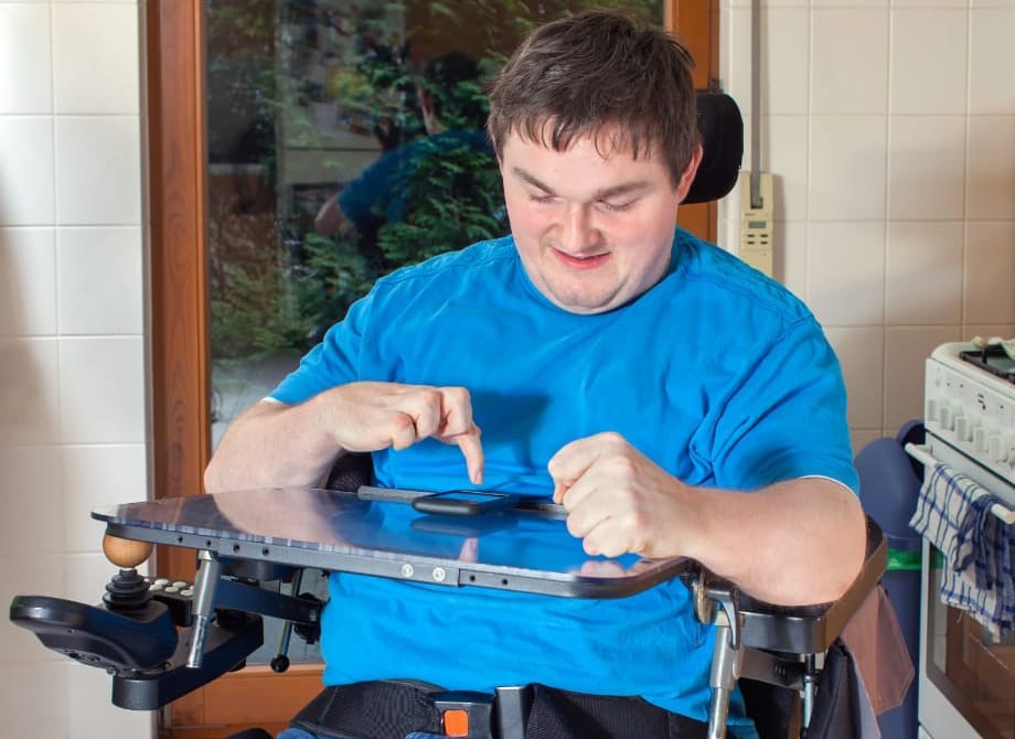 A young white man with cerebral palsy uses his smartphone as he sits in his wheelchair.