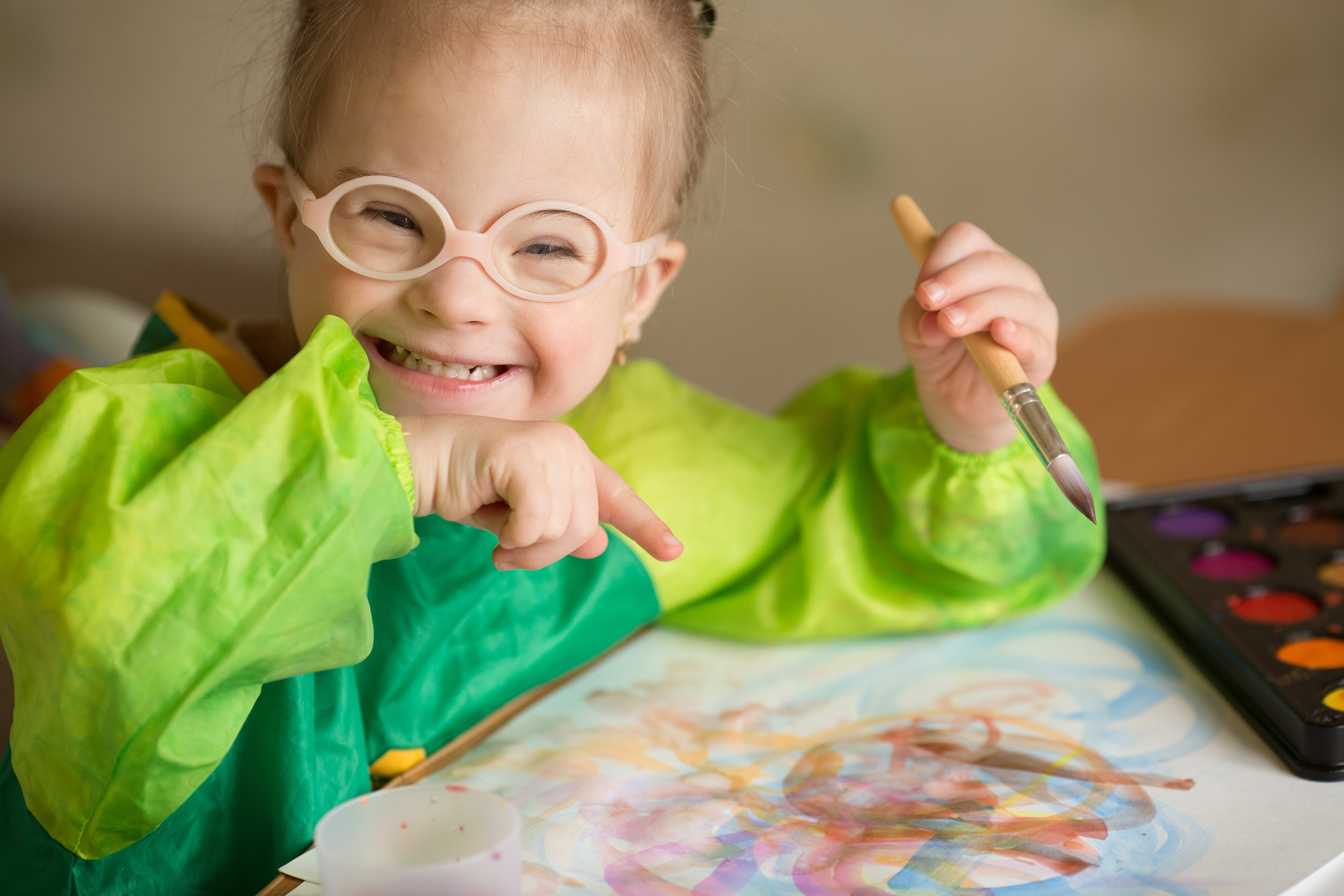 Young white girl with Down syndrome wears glasses and smiles at the camera