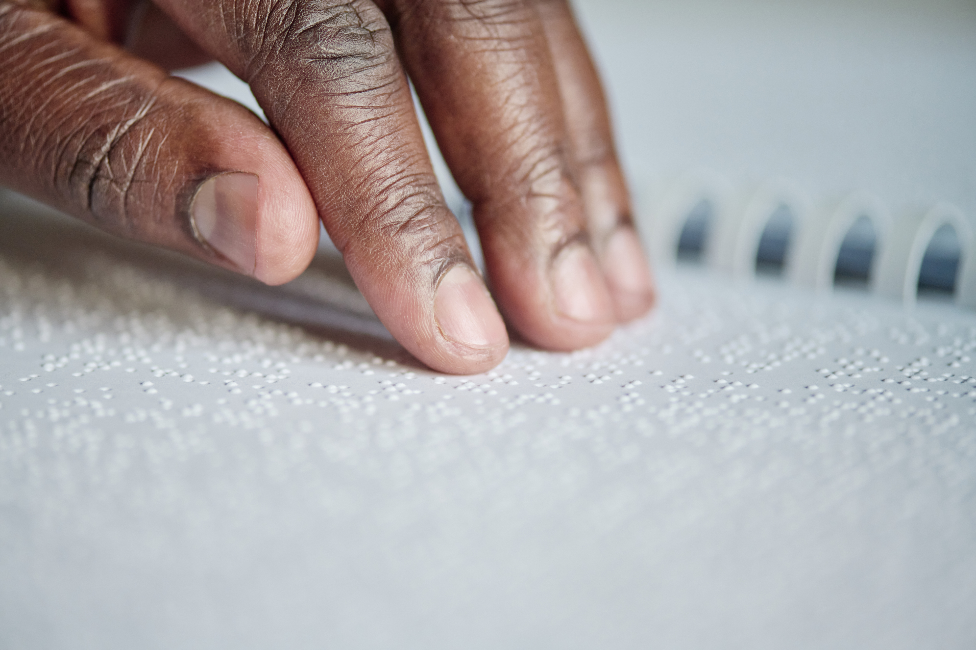 A Black man uses his fingers to read braille