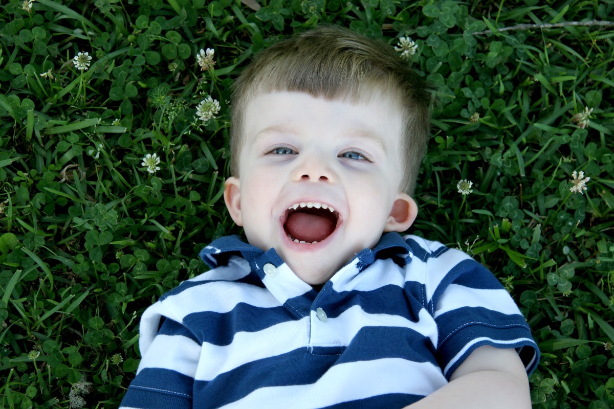 A young white Deaf boy lays in the grass outside and laughs