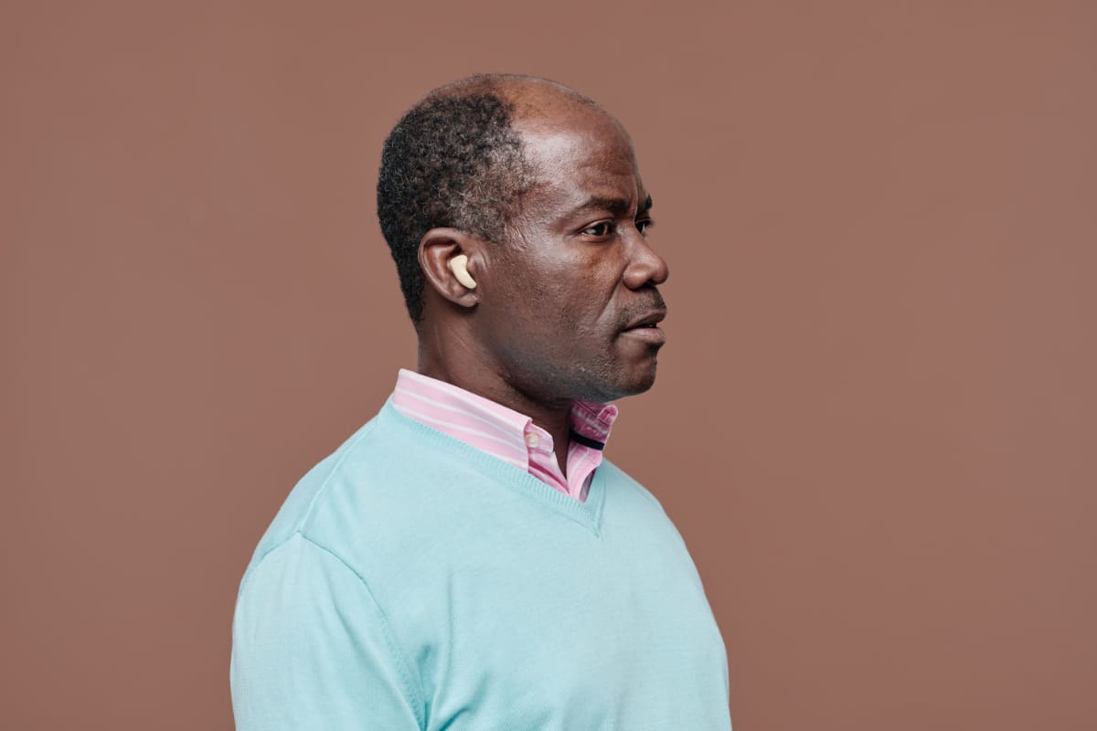 A senior Black man with a hearing aid is shown in profile