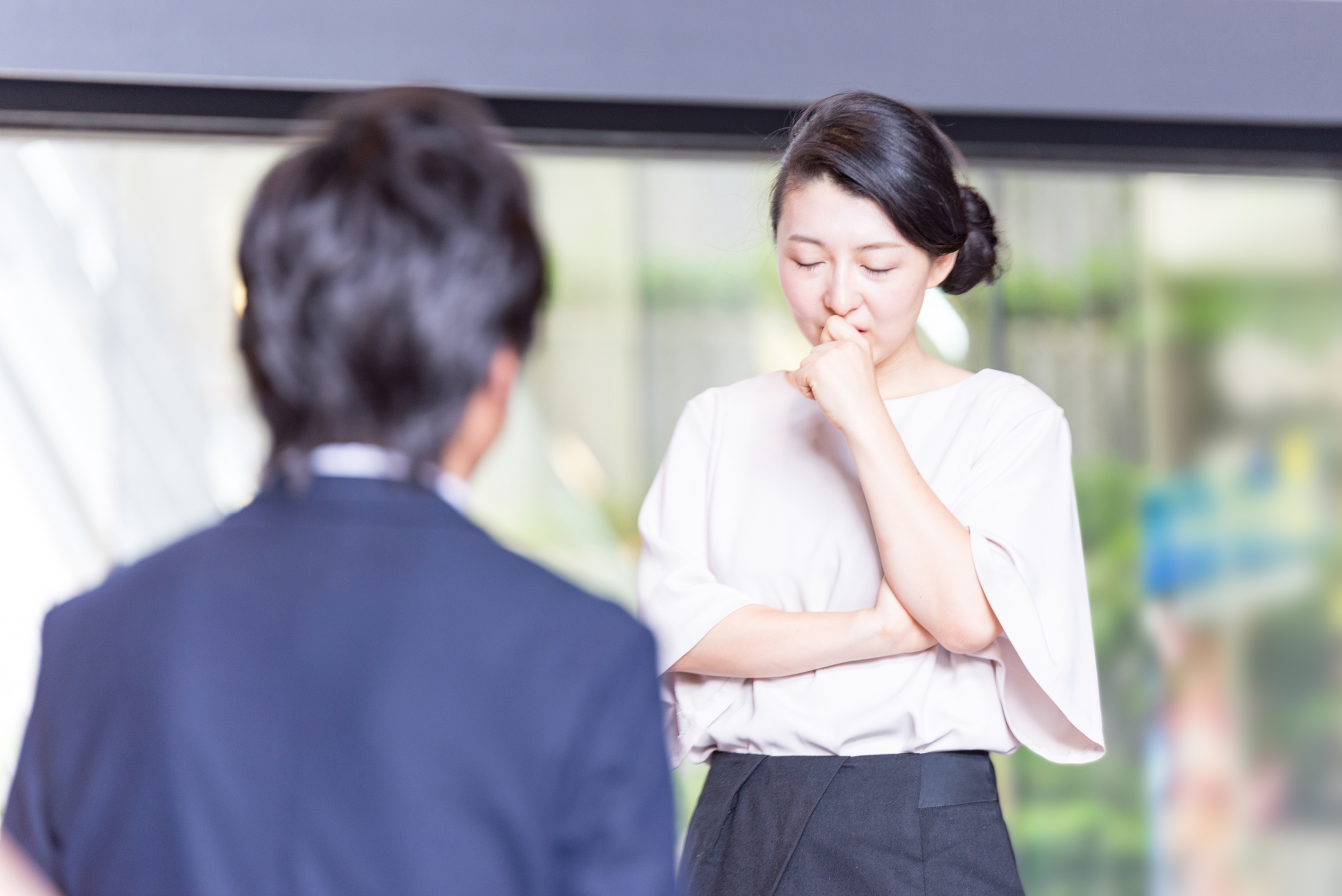 An embarrassed young woman holds her hand to her mouth and stares at the floor during a conversation with a colleague