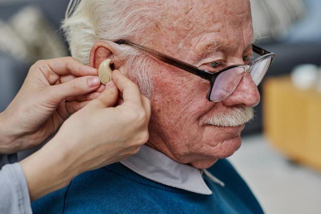 A senior white man with low vision sits in the doctors office as he receives a hearing aid