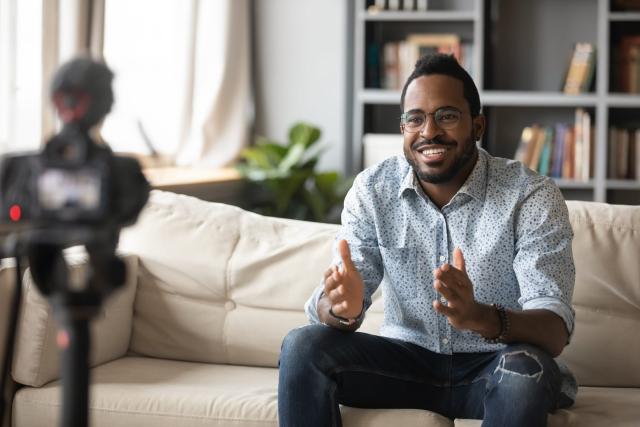 Black man sits on couch recording professional video presentation at home