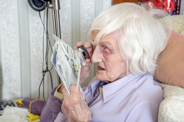 Elderly white woman uses a magnifying loupe to read a pamphlet